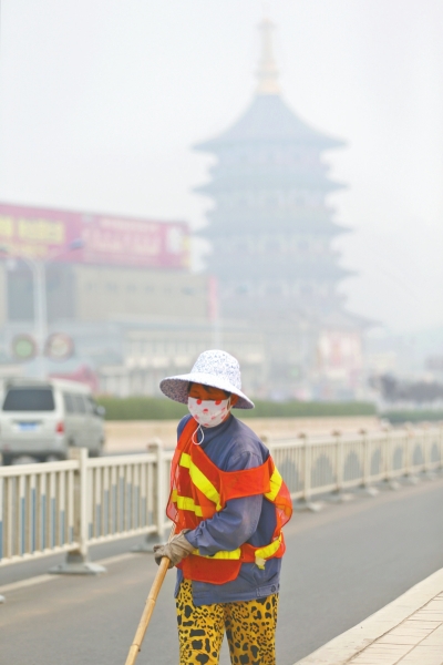 近日，在古都洛陽，環(huán)衛(wèi)工人身后的“天堂”被霧霾籠罩著。