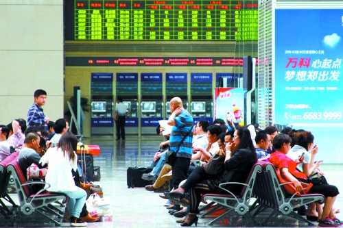 候車(chē)大廳溫度很高，一名乘客一手扇風(fēng)、一手擦汗