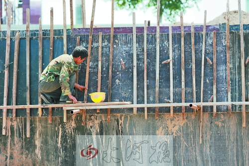 　　烈日下，狹窄的架子上，工人正用錘子固定樁基。