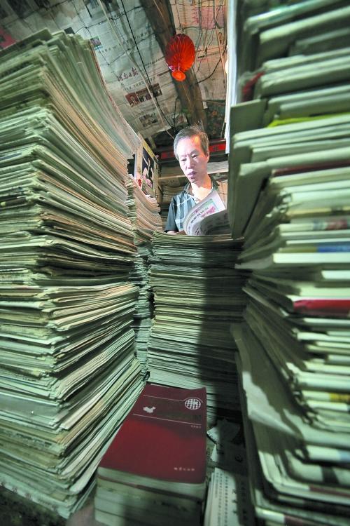 王曉民坐在寫(xiě)字桌前，被報(bào)紙淹沒(méi)。