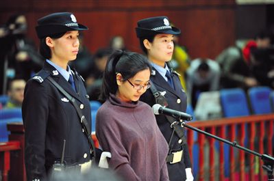 被告人盧梅低著頭，站在朝陽(yáng)法院刑事審判庭的被告席上。